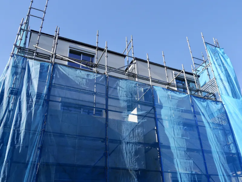 解体工事の開始前に住宅の周囲に設置された足場と、防音・防塵用の紺色の養生シート