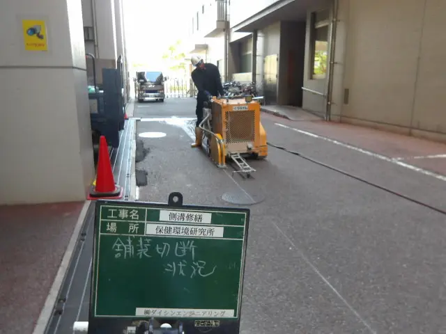 カッター機械を使用して駐車場アスファルトを切断する作業