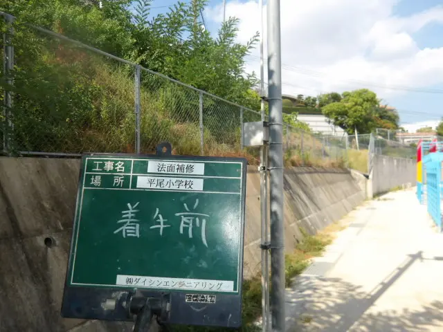 平尾小学校の法面補修前、雑草が繁茂した擁壁上の斜面